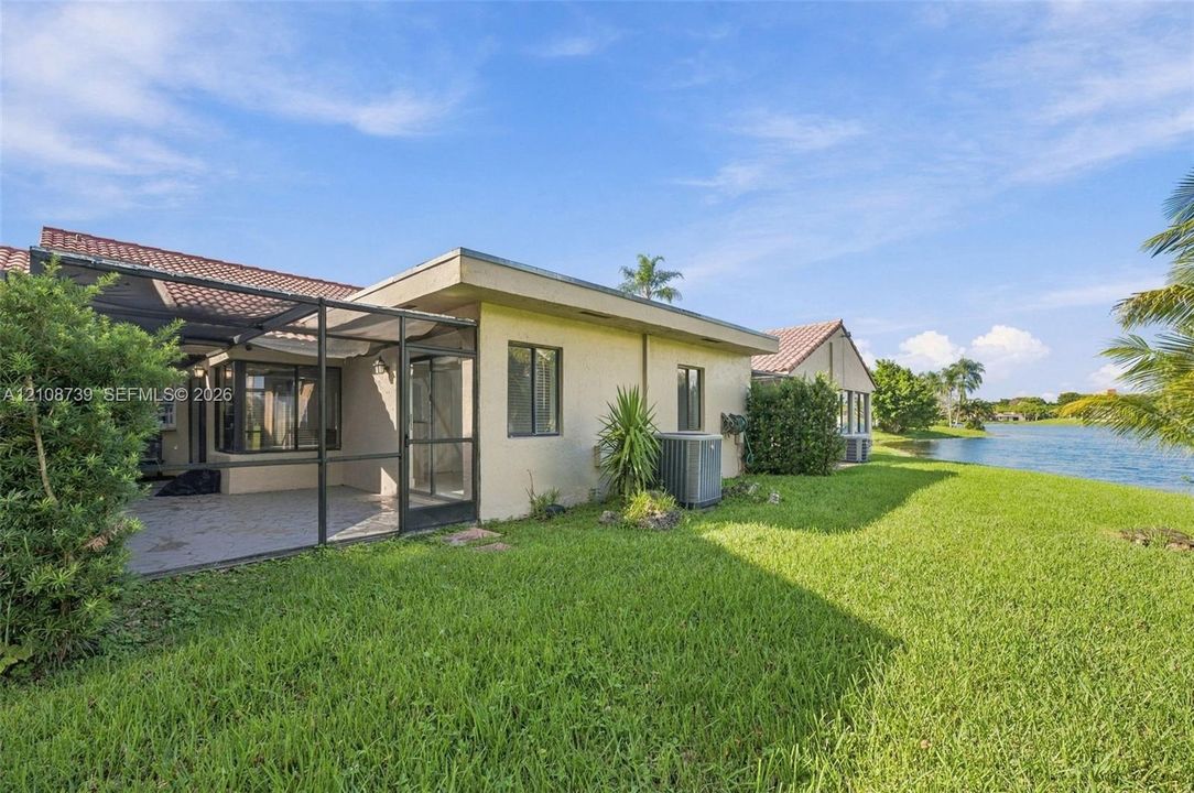 Rear exterior featuring a screened-in lanai, tile roof, stucco siding, and waterfront positioning overlooking the lake