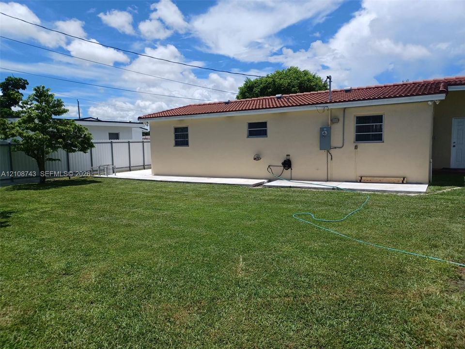 Exterior rear yard featuring a concrete patio, stucco siding, a tiled roof, and perimeter fencing