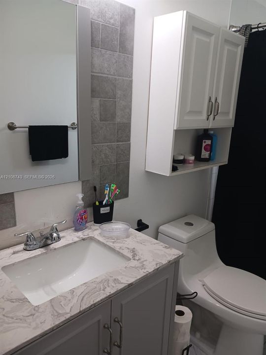 Bathroom vanity featuring a stone-pattern countertop, integrated sink, grey cabinetry with metallic hardware, wall-mounted white storage cabinet, and tiled backsplash