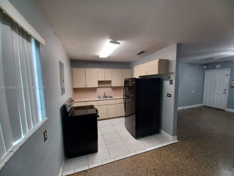 Kitchen featuring light-toned cabinetry, solid-surface countertops with an integrated sink, black appliance package, and tile flooring