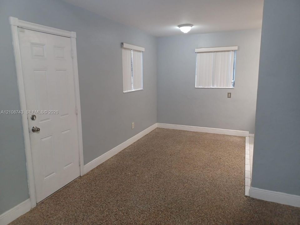 Interior space featuring textured flooring, two windows with vertical blinds, a solid-panel door, and a flush-mount ceiling light fixture