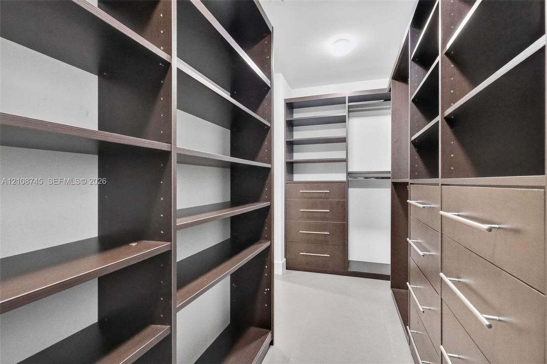 Walk-in closet featuring extensive custom dark-wood cabinetry, adjustable shelving, integrated drawer banks with horizontal hardware, and hanging rods