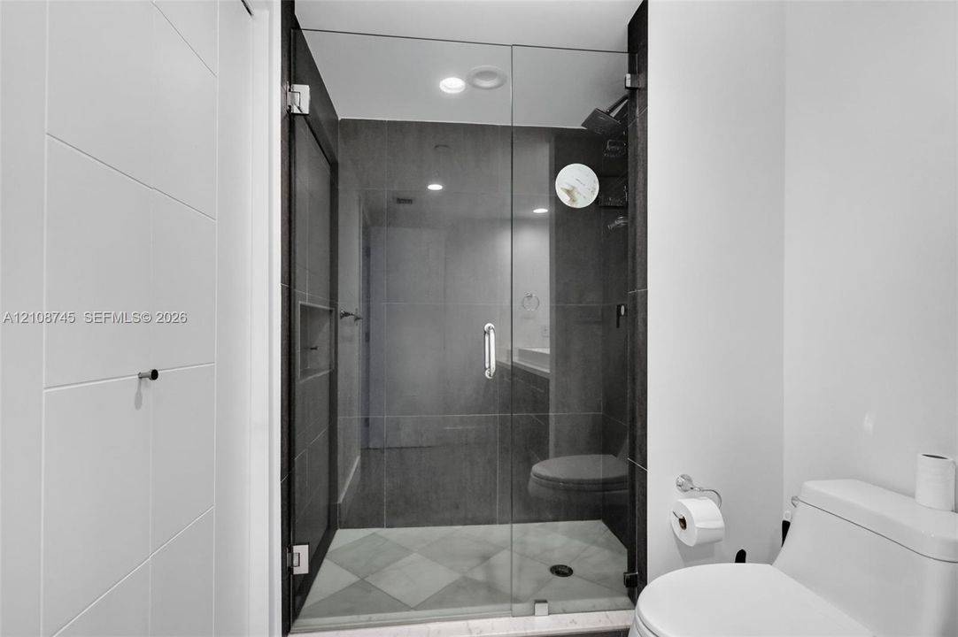 Walk-in shower featuring a frameless glass door, dark wall tile, built-in recessed shelving, a rainfall showerhead, and a diamond-patterned floor tile