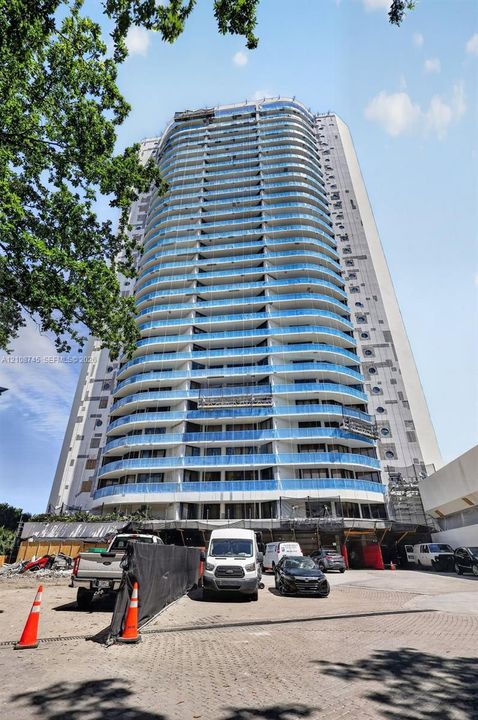 High-rise residential tower featuring a curved facade, light-toned exterior cladding, and stacked balconies with blue glass railings