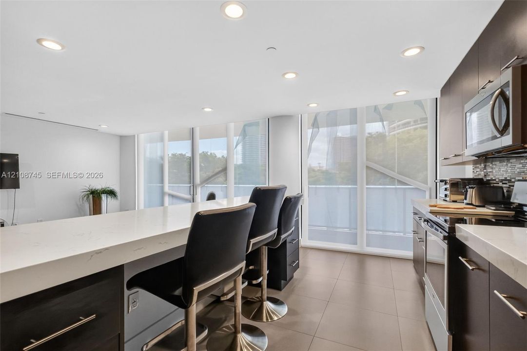 Kitchen featuring dark cabinetry, quartz countertops, tile flooring, recessed lighting, and floor-to-ceiling windows