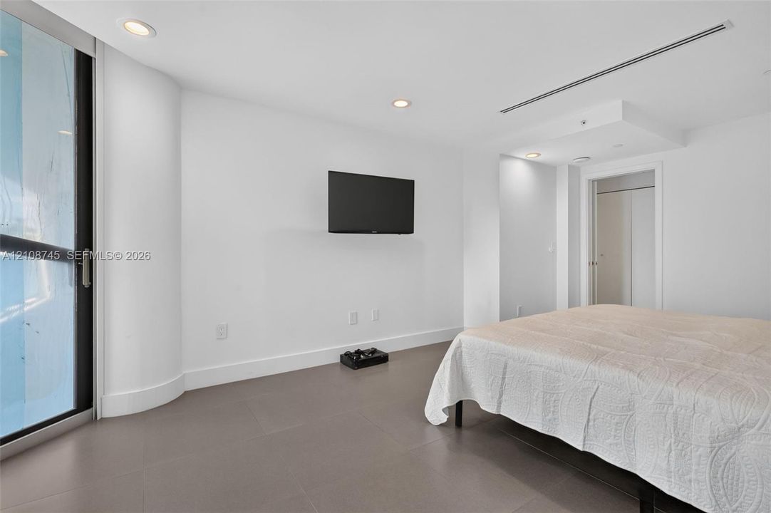 Neutral interior featuring porcelain tile flooring, recessed ceiling lighting, a curved architectural wall detail, and a glass-paneled sliding door