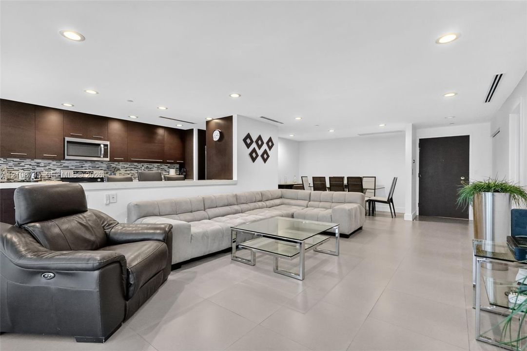 Open-concept space featuring large-format tile flooring, recessed ceiling lighting, dark cabinetry, and a decorative tile backsplash