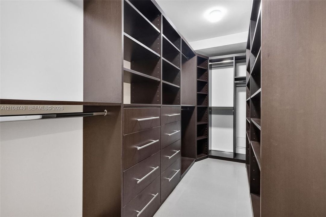 Walk-in closet featuring custom dark-finish cabinetry, floor-to-ceiling shelving, integrated hanging rods, and built-in drawers with polished hardware