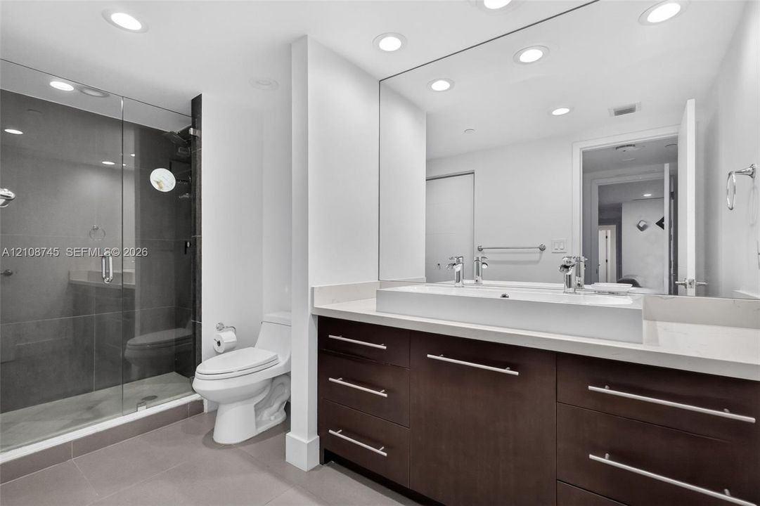 Bathroom featuring a dark wood-finish vanity with a dual-sink stone countertop, a walk-in glass-enclosed shower with tile surround, and recessed lighting