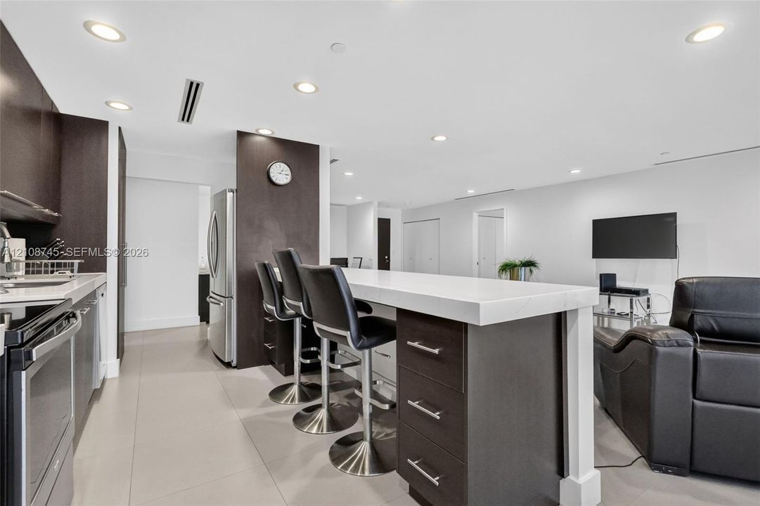 Kitchen featuring dark-finish cabinetry, an extended island with thick-edge countertops, stainless steel appliances, and large-format tile flooring