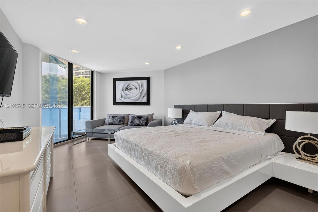 Floor-to-ceiling windows, large-format tile flooring, recessed ceiling lighting, and a dark, paneled built-in headboard