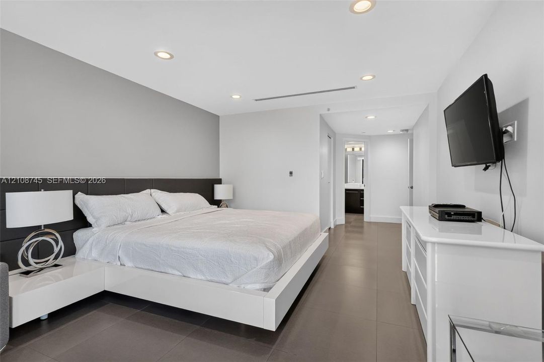 Neutral-toned room featuring large-format tile flooring, recessed ceiling lighting, and a dark integrated headboard panel
