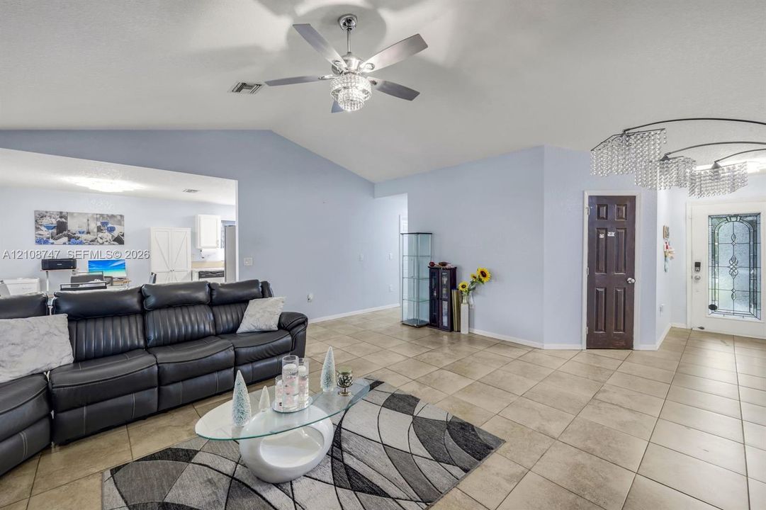 Vaulted ceilings featuring a crystal-accented ceiling fan and a modern multi-tiered chandelier, complemented by large-format tile flooring and an entry door with decorative glass paneling