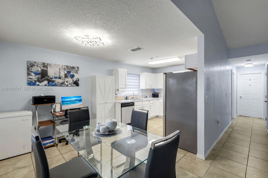 Kitchen featuring white cabinetry, stainless steel refrigerator, dishwasher, and tile flooring throughout the area