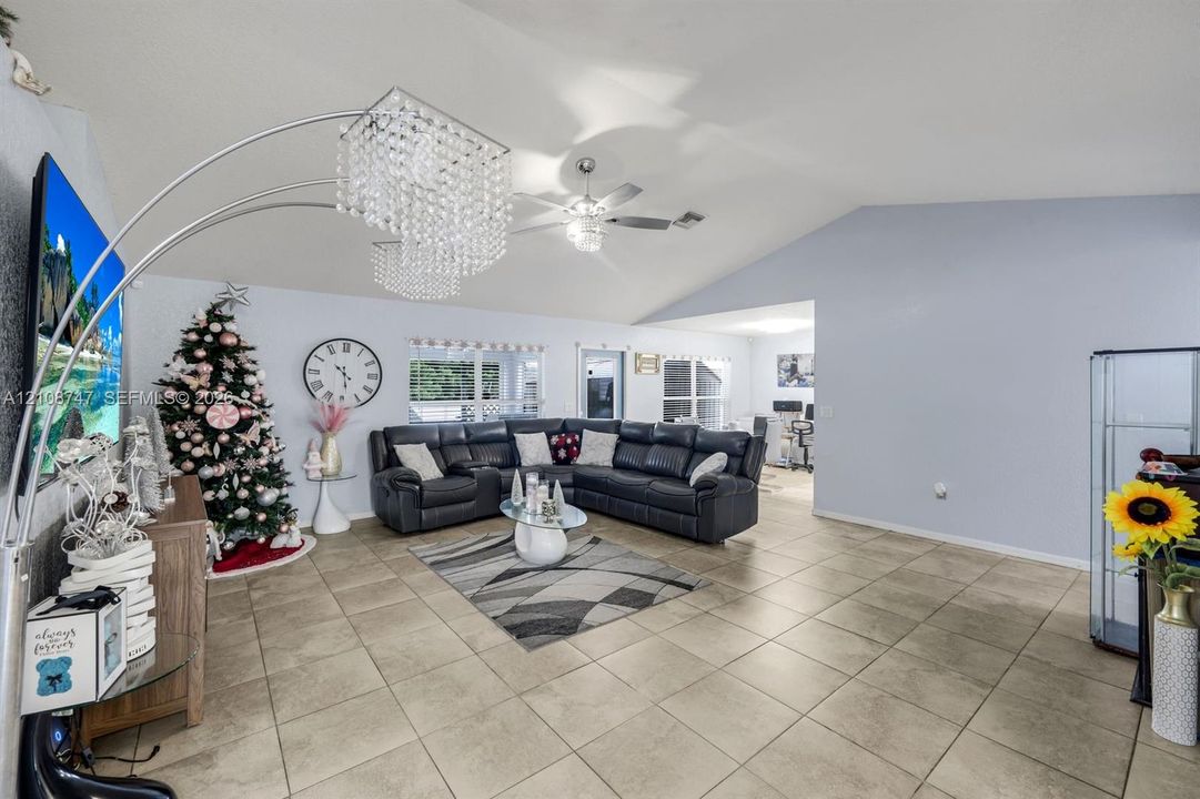Living area featuring vaulted ceilings, neutral ceramic tile flooring, and a multi-blade ceiling fan with integrated lighting