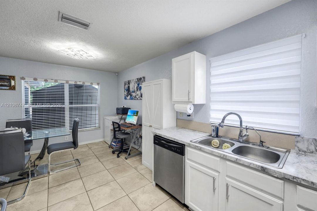 Kitchen featuring white cabinetry, stone-finish countertops, stainless steel dual-basin sink with arched faucet, stainless steel dishwasher, and ceramic tile flooring