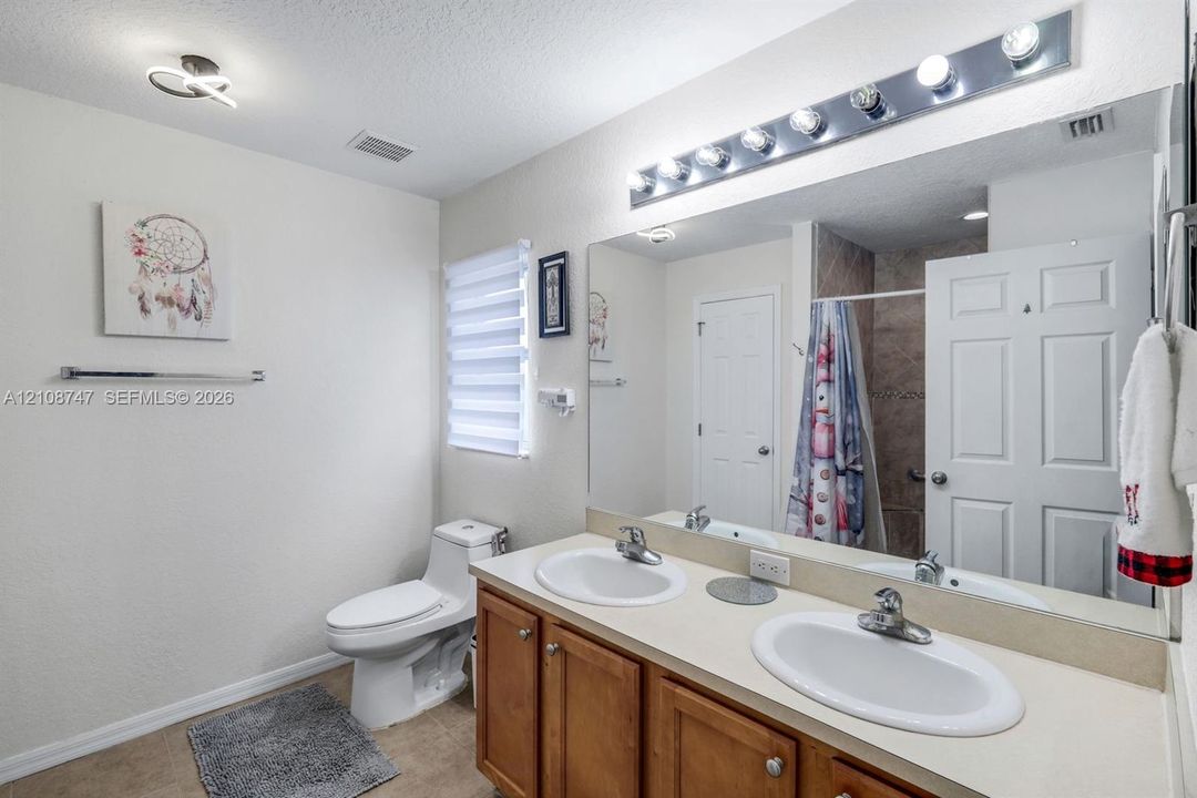 Bathroom featuring a dual-sink vanity with wood cabinetry, a large wall-to-wall mirror, overhead vanity lighting, and a one-piece toilet