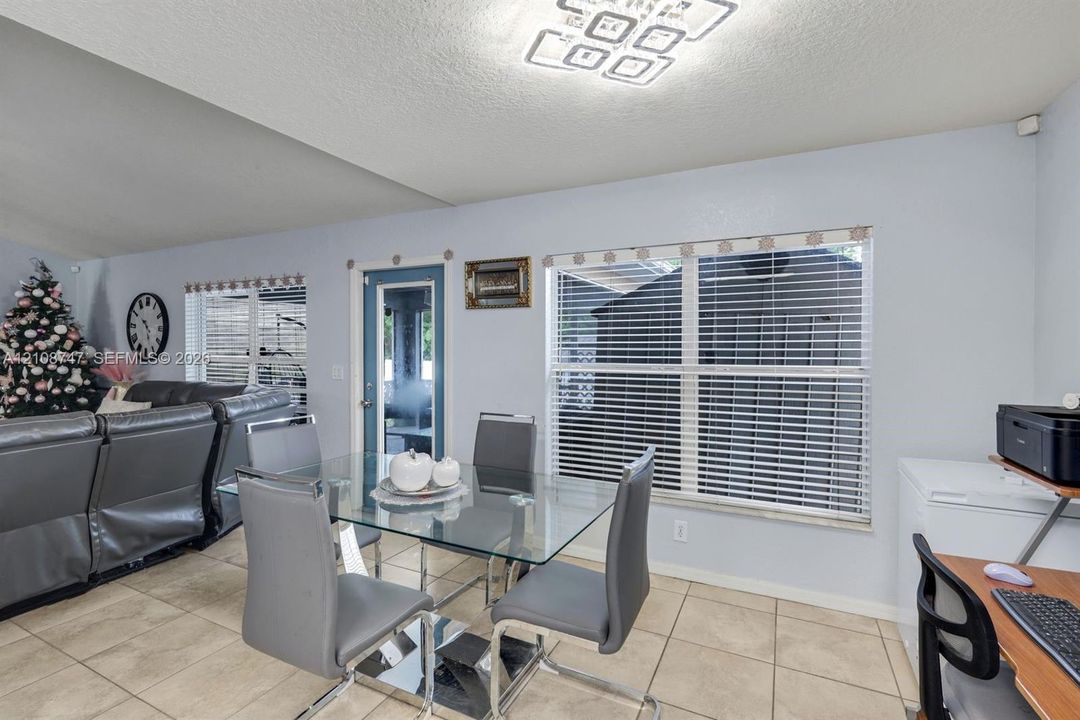 Open-concept area featuring light-toned tile flooring, recessed ceiling design, contemporary geometric light fixture, and multiple windows with horizontal blinds