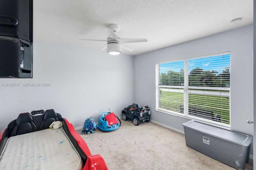 Room featuring neutral wall tones, wall-to-wall carpeting, a multi-blade ceiling fan with integrated lighting, and a large window with horizontal blinds