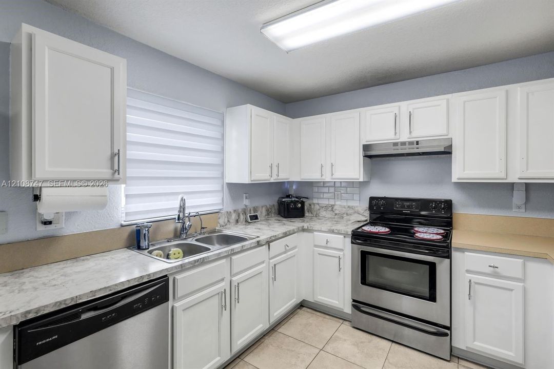 Kitchen featuring white shaker-style cabinetry, stone-patterned laminate countertops, stainless steel appliances, double-basin sink, and tile flooring
