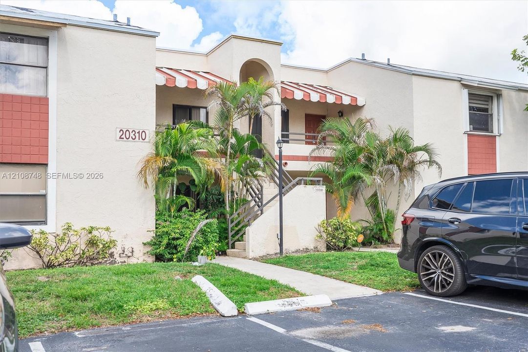Two-story stucco exterior featuring red and white striped awnings, arched architectural detailing, metal railings, and integrated palm landscaping