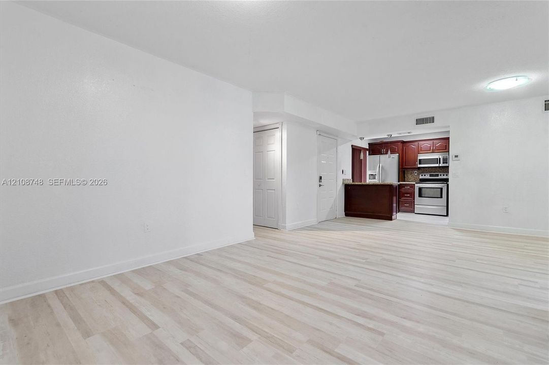 Open-concept area featuring light-toned wood-finish flooring and a kitchen with dark wood-finish cabinetry, stainless steel appliances, and a built-in counter