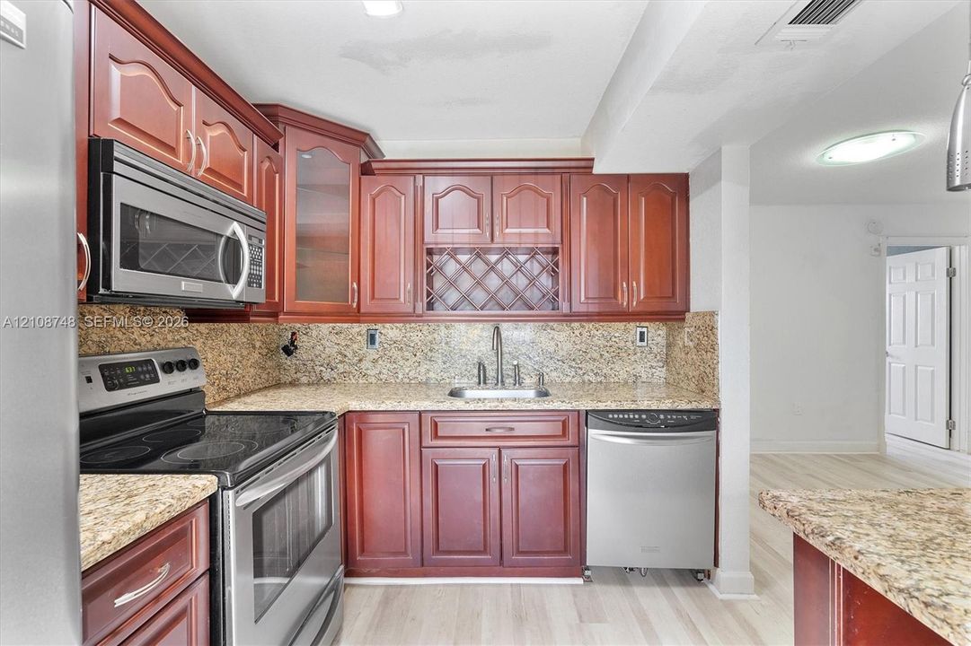 Kitchen featuring stained wood cabinetry, stone-surface countertops, built-in wine rack, stainless steel appliances, and wood-finish flooring