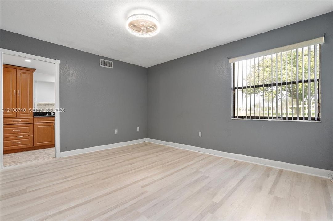 Room featuring wood-finish flooring, neutral gray wall paint, and a circular flush-mount ceiling fixture with integrated fan