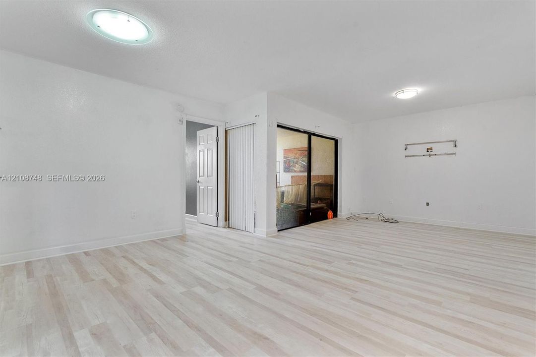Light-toned wood-finish flooring, recessed ceiling lighting, and sliding glass doors with vertical blinds