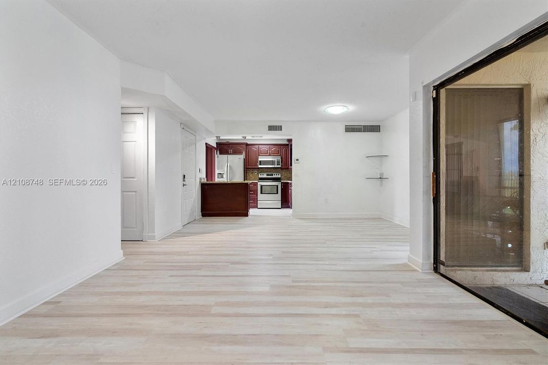 Open-concept floor plan featuring wood-finish flooring, recessed ceiling lighting, kitchen with dark-toned cabinetry, stainless steel appliances, and large sliding glass door