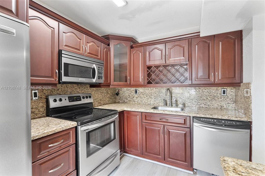 Kitchen featuring stained wood cabinetry, stone countertops, stainless steel appliances, built-in wine rack, and a glass-front upper cabinet