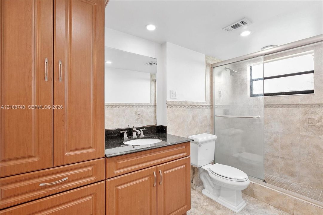 Bathroom featuring wood-finish cabinetry, dark stone vanity countertop, undermount sink, and tiled walk-in shower with sliding glass doors