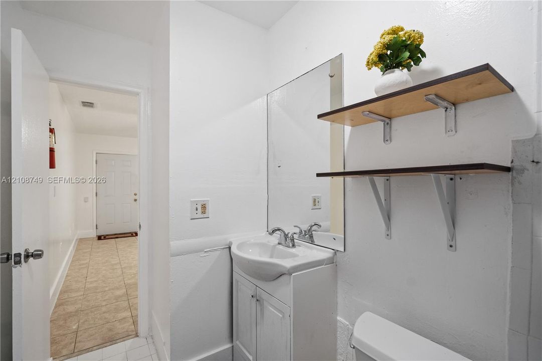 White pedestal-style vanity with a porcelain sink, dual-handle faucet, integrated cabinet storage, wall-mounted rectangular mirror, and two wooden floating shelves with metal brackets