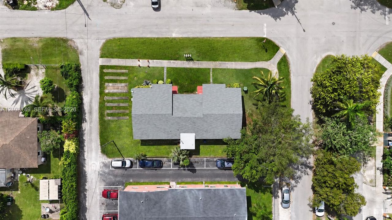 Corner lot property featuring a multi-pitched shingle roof, expansive perimeter lawn, paved off-street parking area, and established mature landscaping