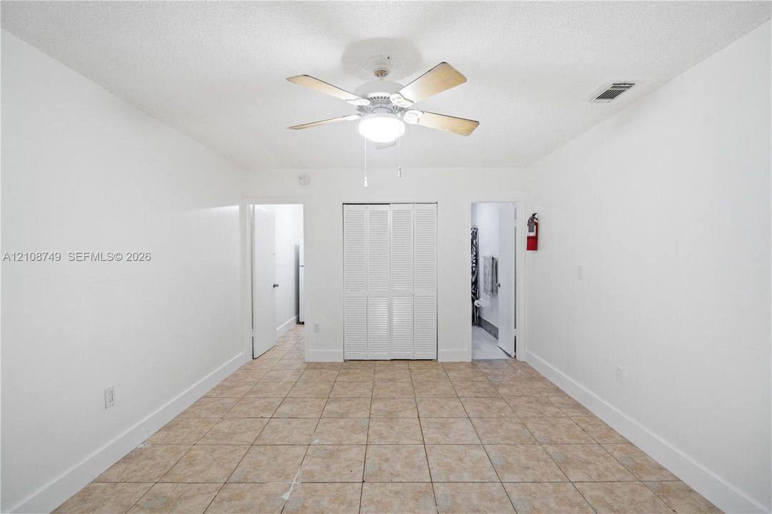 Room featuring neutral tile flooring, white walls, bi-fold closet doors, and a ceiling fan with integrated lighting