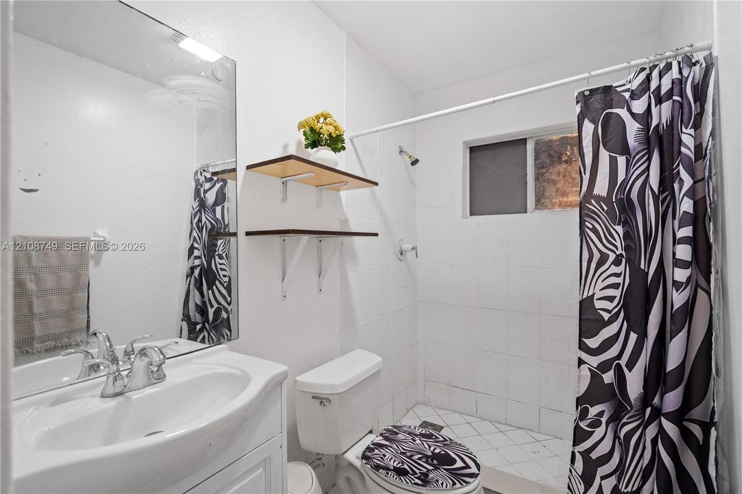 Bathroom featuring a white vanity cabinet, ceramic tile shower surround, wall-mounted shelving, and a frameless mirror