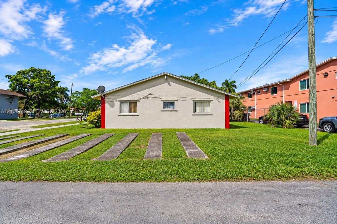Single-story exterior featuring a light-toned stucco facade with red vertical accents, a gabled roofline, and dedicated concrete slab parking strips