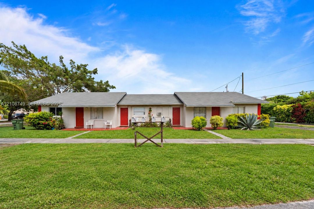 Single-story exterior featuring a gray shingle roof, light-toned stucco siding, vibrant red entry doors, and mature landscaping