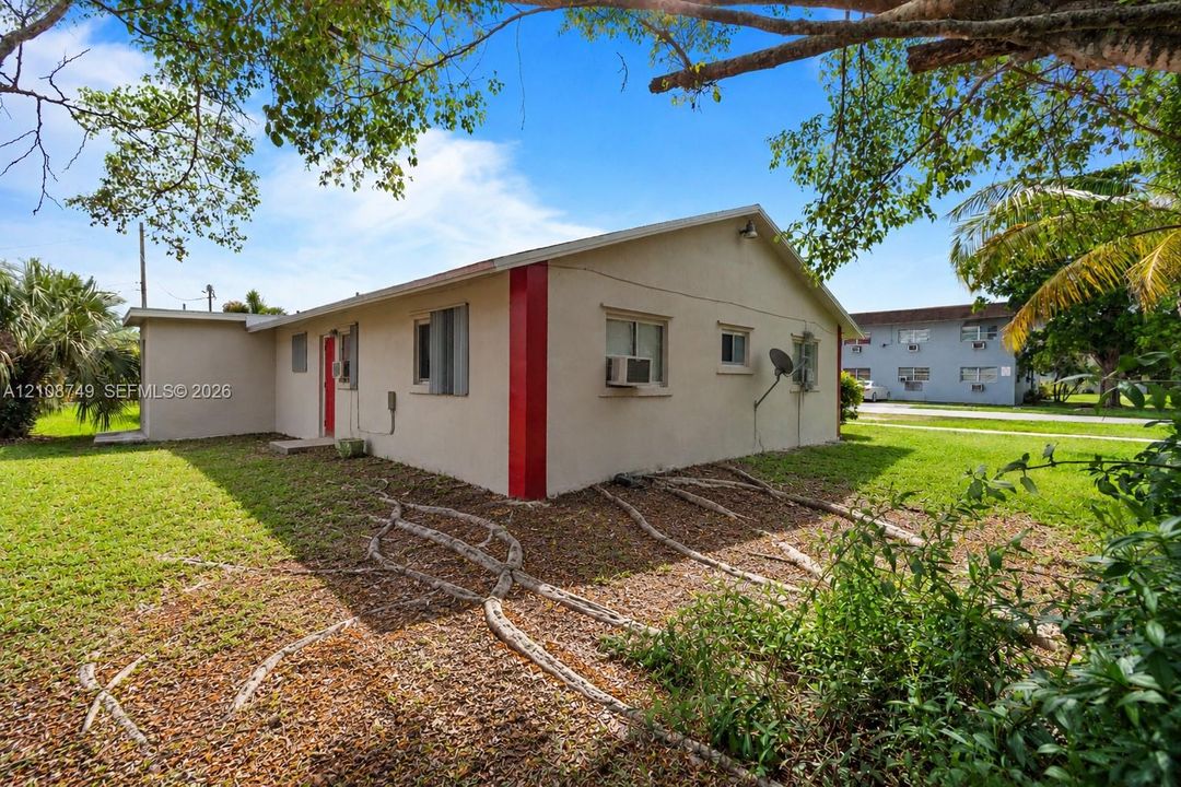 Stucco exterior featuring a low-slope roof, concrete foundation, and mature trees on the surrounding lot