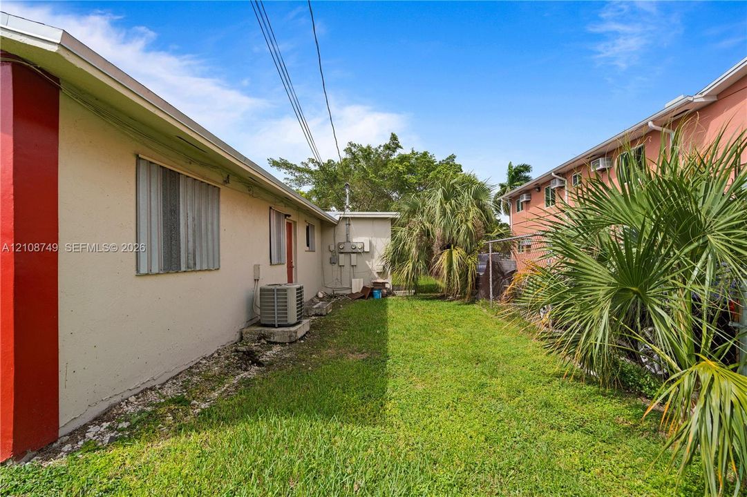 Stucco exterior walls, metal storm shutters, and open lawn area with palm trees