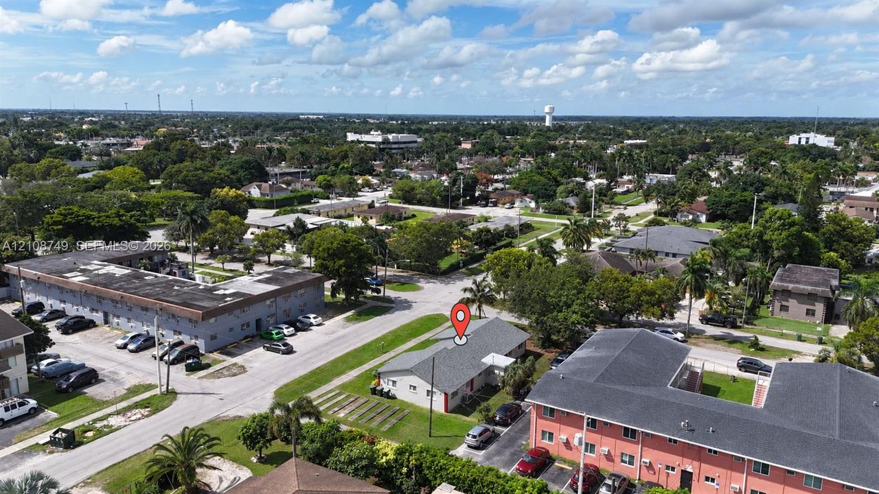 Aerial perspective of a single-story residence featuring a shingled roof, asphalt driveway, and surrounding lawn area situated within an established residential neighborhood