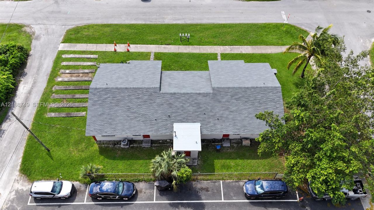 Aerial view featuring a multi-segment shingle roof, established landscaping, and dedicated asphalt parking stalls