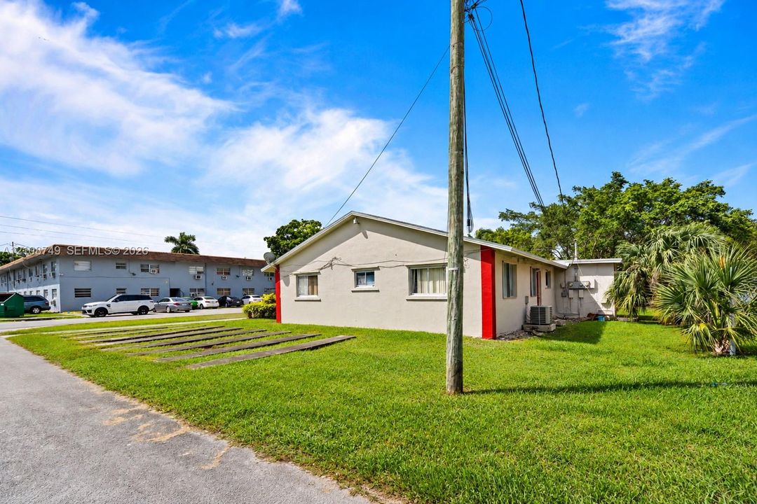 Single-story residence featuring a neutral stucco exterior with red corner accents, a pitched roof, and a lawn with integrated concrete parking runners