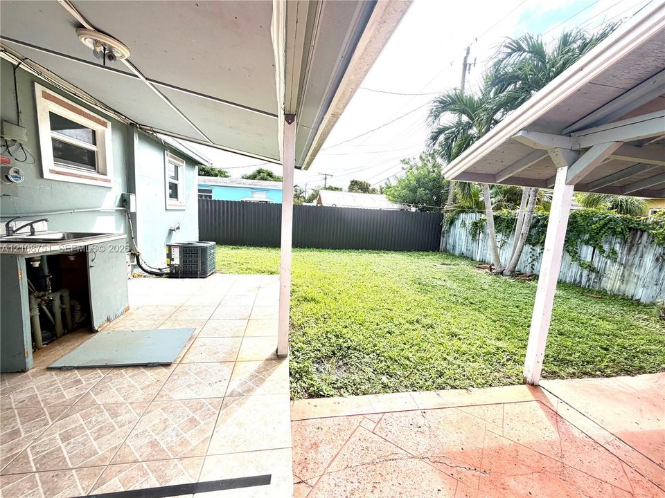 Covered patio with integrated outdoor sink station, concrete tile flooring, and enclosed backyard featuring perimeter fencing and mature palm trees