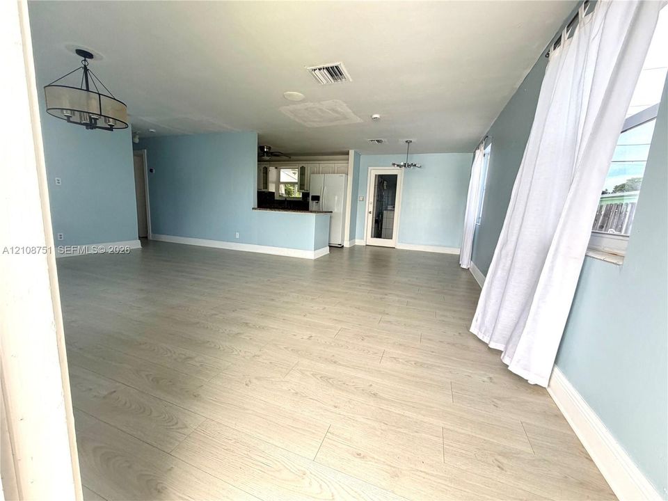 Open-concept interior featuring light-toned wood-finish flooring, a kitchen breakfast bar, and multiple drum-style ceiling light fixtures