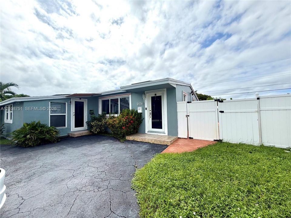 Single-story exterior featuring painted siding, white-trimmed glass paneled entry doors, an asphalt driveway, and a white privacy fence