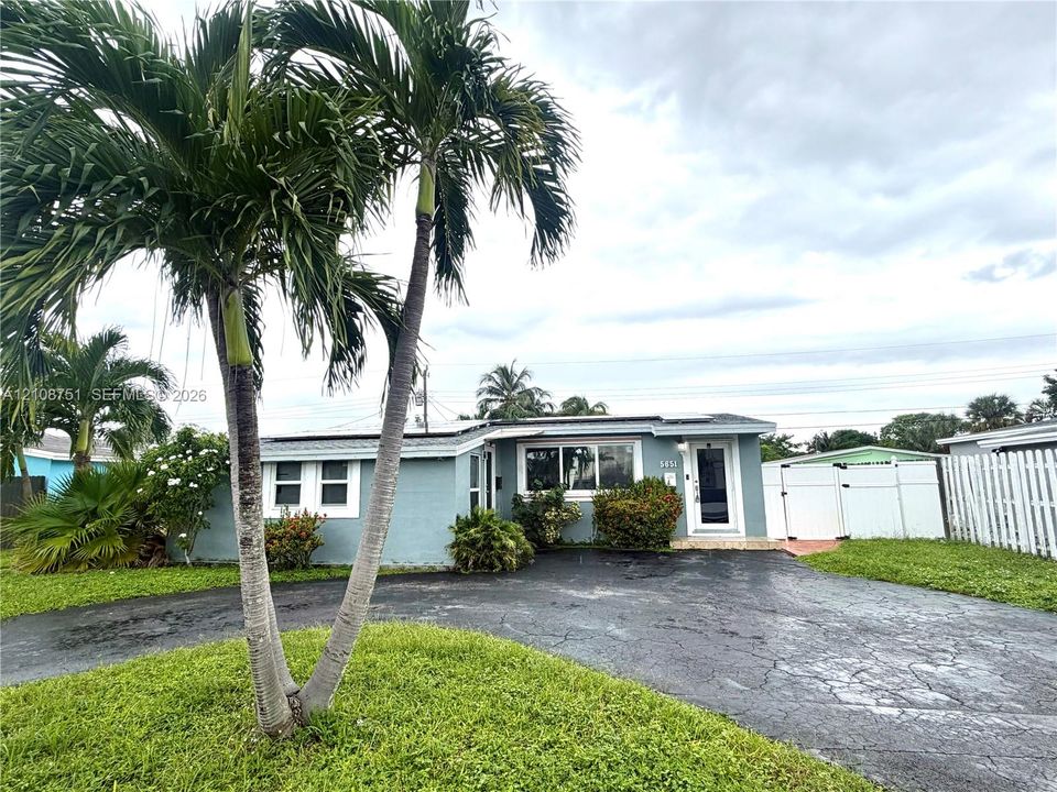 Exterior featuring a light blue stucco finish, asphalt driveway, solar panels, and white vinyl privacy fencing