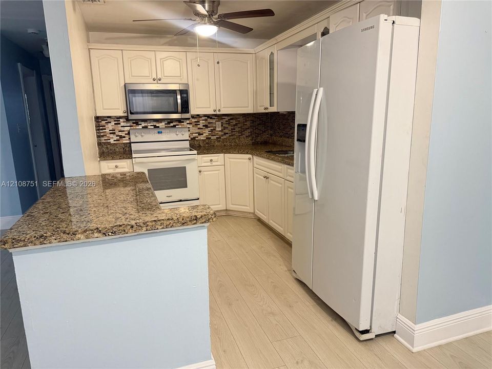 Kitchen featuring off-white cabinetry, stone-finish countertops, a multi-tone tile backsplash, built-in stainless steel microwave, and wood-finish flooring