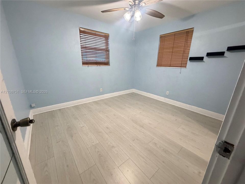 Room featuring wood-finish flooring, a ceiling fan with light fixture, and two windows with horizontal blinds