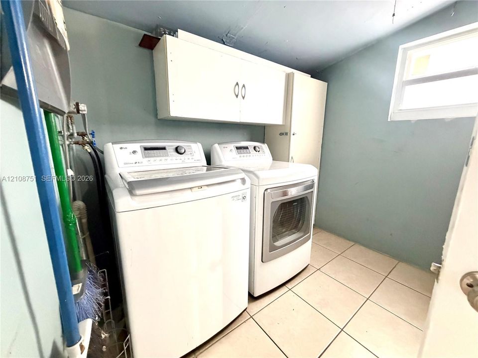 Laundry room featuring ceramic tile flooring, white built-in cabinetry, and a window for natural light